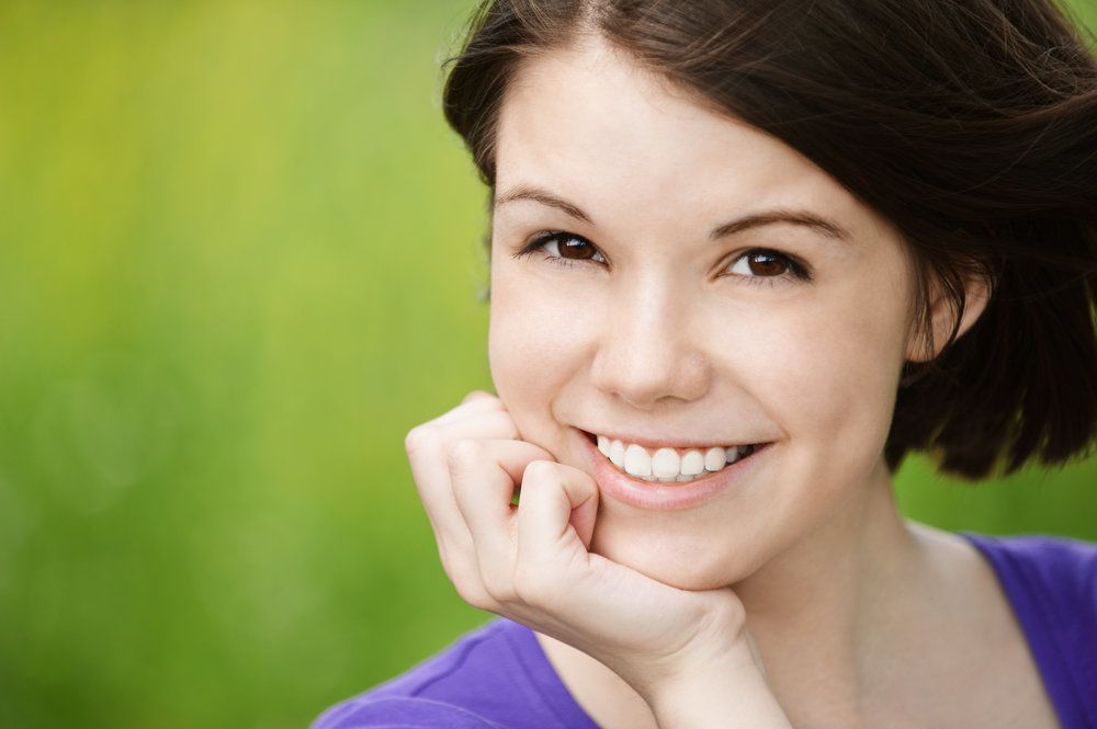 Smiling young woman posing for picture with chin resting on hand